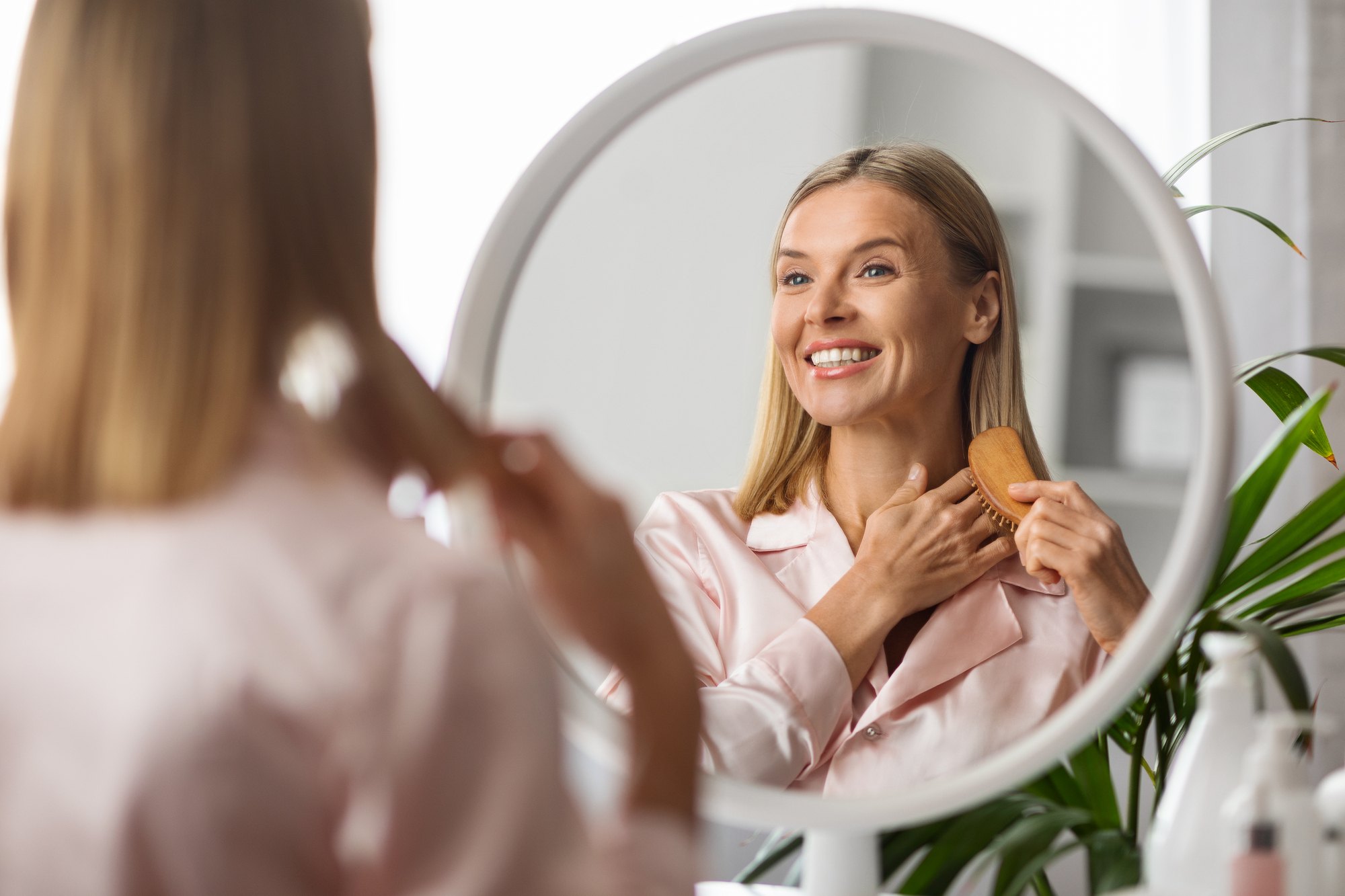 woman-smiling-brushing-hair-mirror